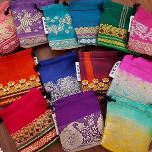 May include: Assortment of colorful drawstring pouches with intricate patterns and gold accents. The pouches are made of fabric and have a drawstring closure. The pouches are labeled with the word "Gems".