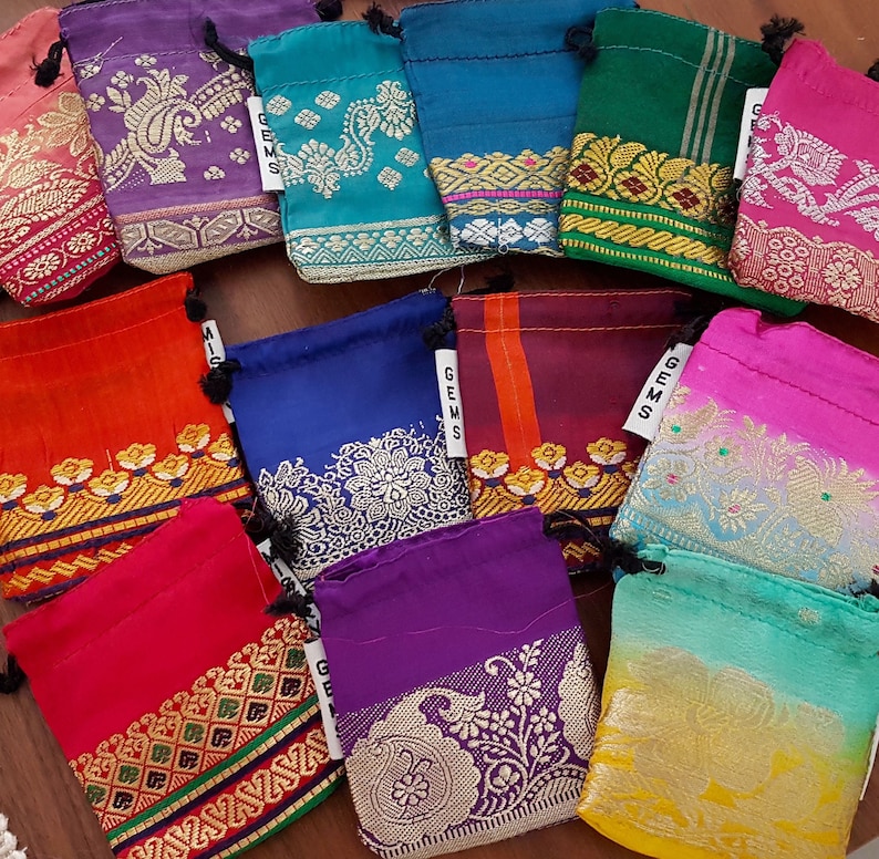 May include: Assortment of colorful drawstring pouches with intricate patterns and gold accents. The pouches are made of fabric and have a drawstring closure. The pouches are labeled with the word "Gems".