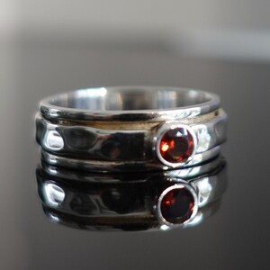 Puede incluir: Un anillo giratorio de plata con textura martillada y una piedra preciosa roja.