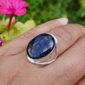 Pode incluir: Um anel de prata com uma grande pedra preciosa oval azul. A pedra preciosa tem uma textura brilhante e salpicada.