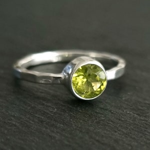 Op de afbeelding: Een zilveren ring met een ronde, lichtgroene edelsteen in een bezel-setting.
