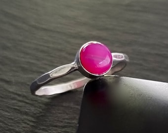 Könnte beinhalten: Ein silberner Ring mit einem rosafarbenen Achat-Edelstein. Der Ring hat eine gehämmerte Textur und ist mit einem runden Cabochon-Stein besetzt.