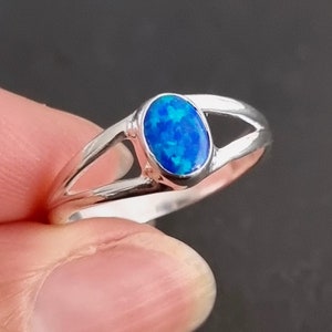 May include: A silver ring featuring a blue oval opal gemstone. The ring has a simple design with a split band.