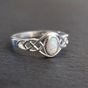 May include: A silver ring with a Celtic knot design and an oval opal gemstone.