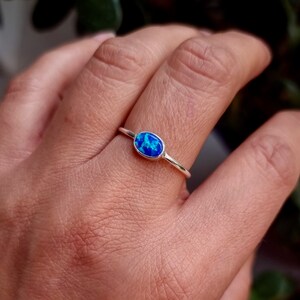 May include: A silver ring with a blue oval opal gemstone. The ring is on a person's finger.