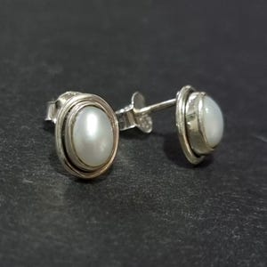May include: A pair of silver earrings with white pearl-like stones set in a silver bezel.