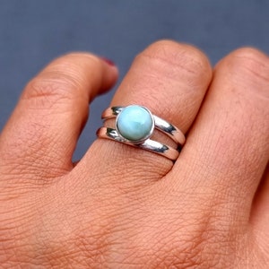 May include: A silver ring with a light blue gemstone set in a double band.