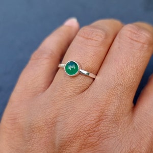 Op de afbeelding: Een zilveren ring met een ronde groene edelsteen. De ring zit aan een vinger.