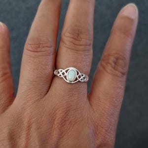 May include: A silver ring with a white opal stone set in a Celtic knot design.
