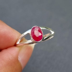 May include: A silver ring featuring a red oval gemstone. The ring has a simple design with a split band.
