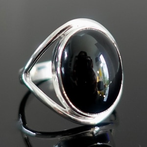 May include: A silver ring with a black oval gemstone set in a bezel setting. The ring has a delicate, openwork design.