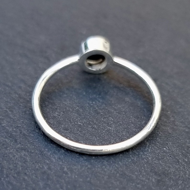 K&ouml;nnte beinhalten: Ein silberner Ring mit einem runden, schwarzen Edelstein in der Mitte. Der Ring ist schlicht und elegant.
