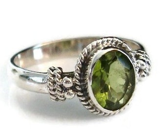 May include: A silver ring with a green oval gemstone. The ring has a rope-like design around the stone and on the band.