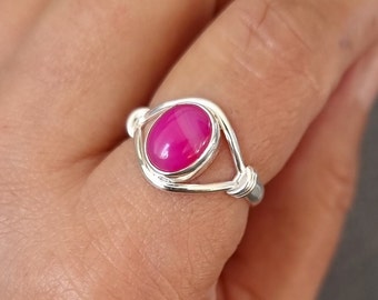 Könnte beinhalten: Ein silberner Ring mit einem rosafarbenen ovalen Edelstein, der in einem drahtgewickelten Design gefasst ist.