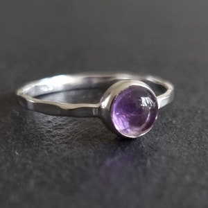 May include: A silver ring with a round, purple amethyst gemstone.