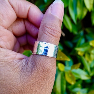 Op de afbeelding: Een brede zilveren ring met een gehammerde textuur. De ring wordt op de duim gedragen.