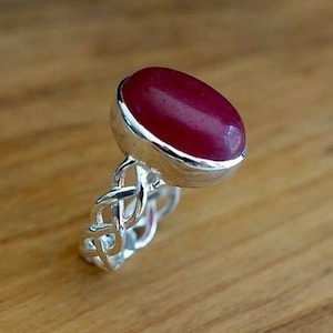 May include: A silver ring with a red oval gemstone set in a Celtic knot design.