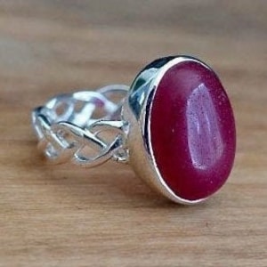May include: A silver ring featuring a Celtic knot design and a large oval red gemstone.