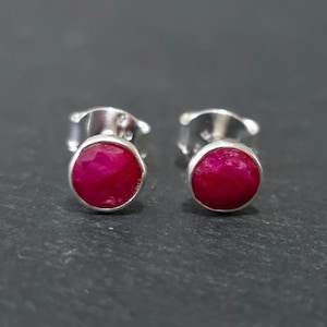 Può includere: Un paio di orecchini a lobo con pietre preziose di rubino rotonde, sfaccettate e di un rosso rosato intenso, incastonate in montature di metallo color argento lucido. Ogni orecchino include un meccanismo a perno standard.