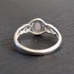 May include: A silver ring with a delicate Celtic knot design and a pink opal gemstone in the center.