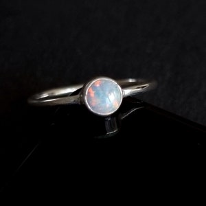 K&ouml;nnte beinhalten: Ein silberner Ring mit einem wei&szlig;en Opal-Edelstein. Der Ring ist schlicht und elegant.