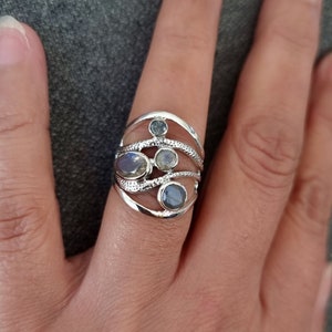 Può includere: Un anello d'argento con un design delicato che presenta più pietre preziose di forma ovale. L'anello ha una fascia testurizzata e un design unico e fluido.