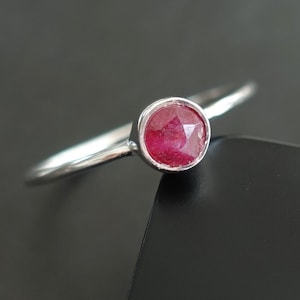 May include: A silver ring featuring a red ruby gemstone. The ring is simple and elegant.