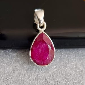 May include: A teardrop-shaped pendant with a deep red ruby gemstone set in sterling silver.
