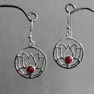 Könnte beinhalten: Ein Paar silberne Ohrringe mit einem roten Edelstein in der Mitte jedes Ohrrings. Die Ohrringe sind in Form einer Lotusblume gestaltet.