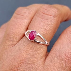 May include: A silver ring with a red oval gemstone set in the center. The ring has a delicate, open design.