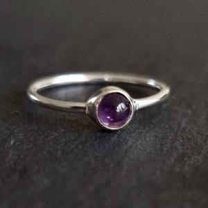 May include: A simple silver ring with a small, round, purple amethyst gemstone.
