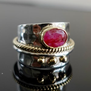 Può includere: Un anello in argento e oro con una pietra ovale rosa. L'anello ha una fascia testurizzata e un design a corda attorno alla parte superiore.