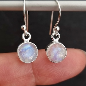 May include: A pair of silver dangle earrings with round moonstone gemstones. The earrings have a simple design and are perfect for everyday wear.