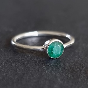 May include: A silver ring with a round, green emerald gemstone.