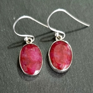 Könnte beinhalten: Ein Paar silberne Ohrringe mit ovalen roten Rubin-Edelsteinen.