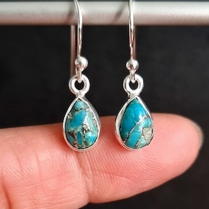 May include: A pair of silver teardrop earrings with turquoise stones. The stones have a marbled pattern of blue and green.