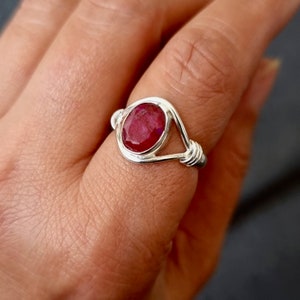 May include: A silver ring with a red ruby gemstone set in a wire-wrapped design.