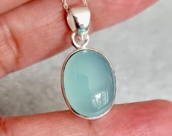 May include: A silver pendant featuring a light blue oval chalcedony gemstone. The pendant is on a silver chain.