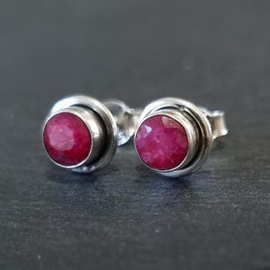 Puede incluir: Un par de pendientes de plata con una piedra preciosa de rubí rojo en cada uno. Los pendientes tienen un diseño sencillo con una piedra redonda engastada en un engaste de plata.