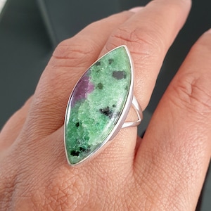 Op de afbeelding: Een zilveren ring met een ovale, groen-roze edelsteen. De edelsteen heeft een uniek patroon van groen, roze en zwart.