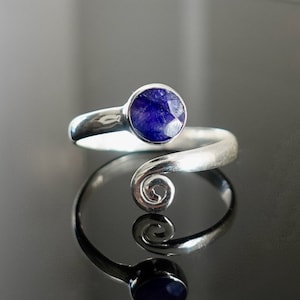 Pode incluir: Um anel de prata com uma gema azul engastada em um engaste de bezel. O anel tem uma banda torcida com um design em espiral.
