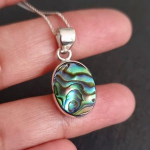 May include: A silver pendant necklace with an oval-shaped abalone shell inlay. The shell has a green, blue, and iridescent color pattern.