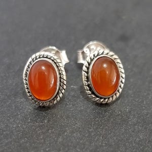 May include: A pair of sterling silver earrings with orange carnelian gemstones. The earrings have a rope-like design around the edges of the gemstones.