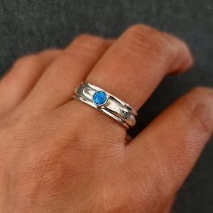 May include: A silver ring with three bands and a blue opal gemstone in the center.