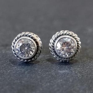 Peut inclure: Une paire de boucles d'oreilles en argent avec une pierre ronde transparente sertie dans un motif de corde.