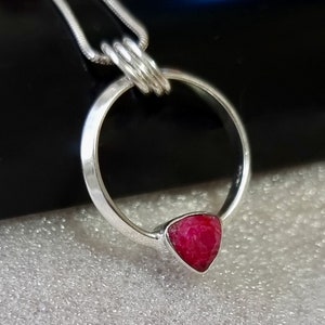 May include: A silver pendant necklace with a circle design and a triangular ruby gemstone.