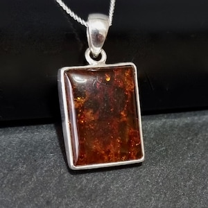 May include: A silver pendant featuring a rectangular amber stone. The amber is a deep orange colour with brown and black inclusions.