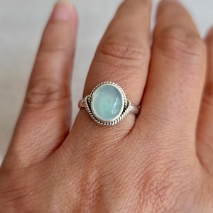 May include: A silver ring with a light blue gemstone set in a rope-like design.
