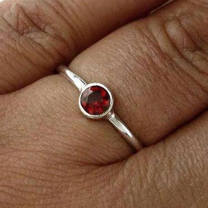 May include: A simple silver ring with a small, round, red gemstone.
