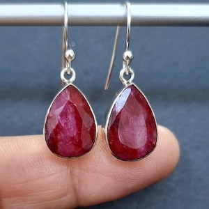 May include: A pair of sterling silver drop earrings featuring teardrop-shaped red ruby gemstones.